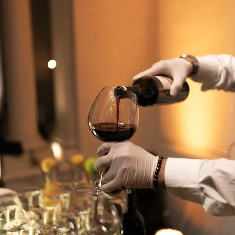 White-gloved sommelier pouring red wine at a private event